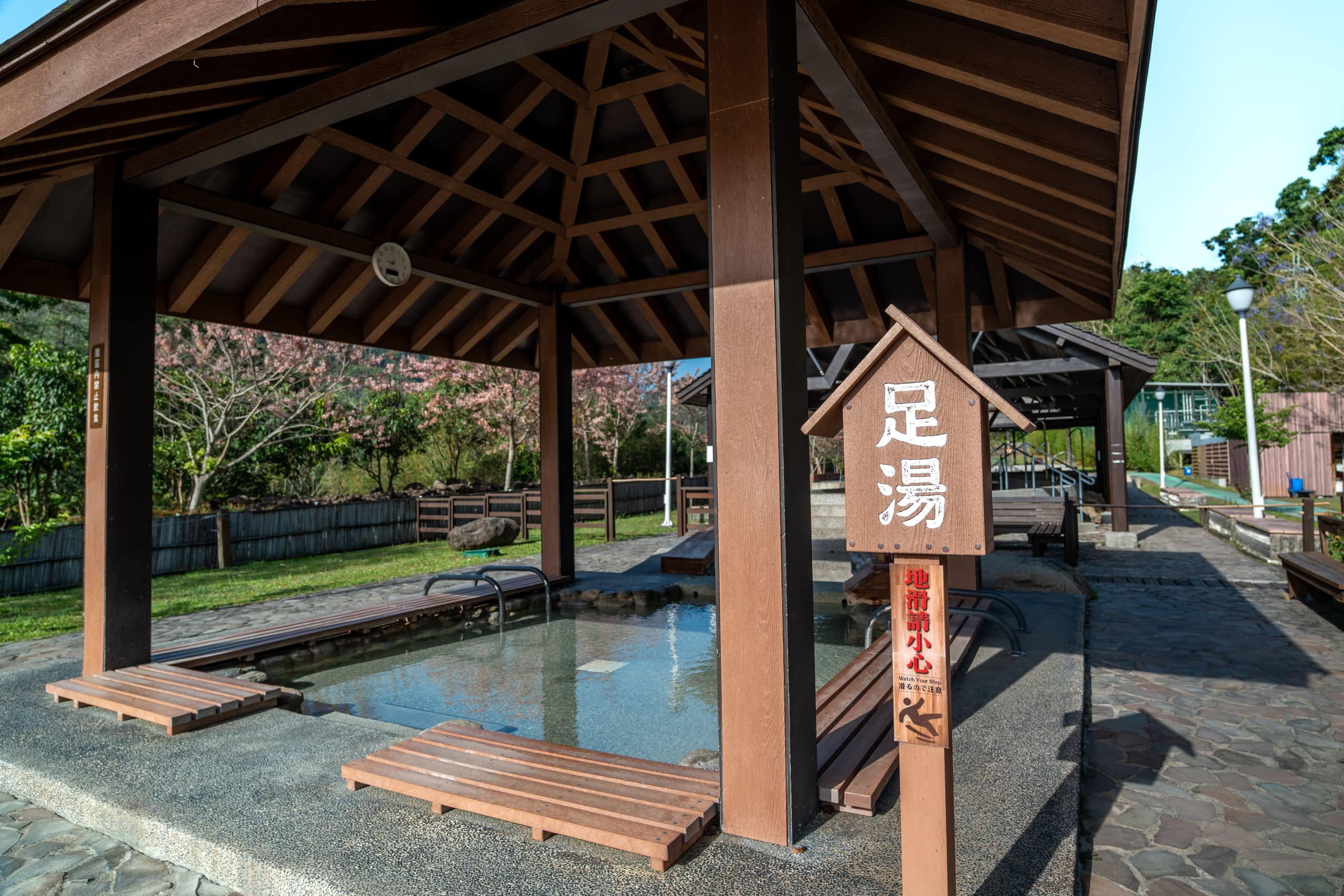 知本溫泉區的公共足湯，木亭下立著「地滑請小心」的告示——雨天泡湯，腳步放慢一點（實景）